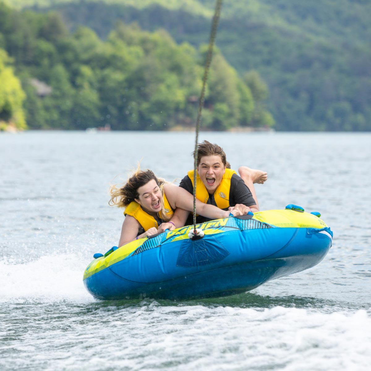 Two girls yell as they try to hold onto a quickly moving inner tube on a lake, at Snowbird Wilderness Outfitters.